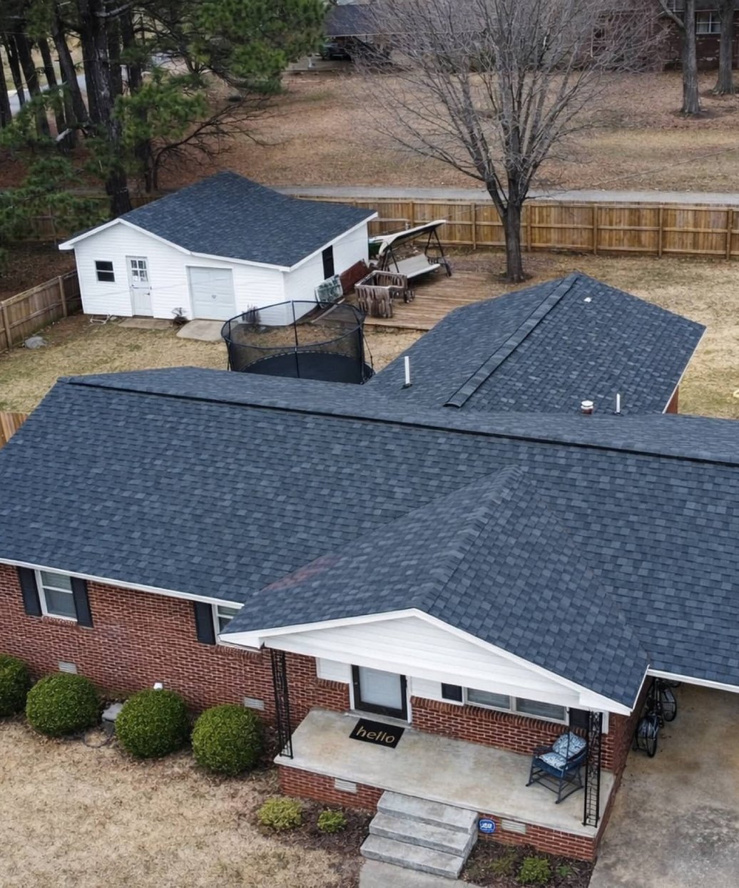 Aerial view of a completed grey shingle roof on a brick ranch home with a new wood privacy fence