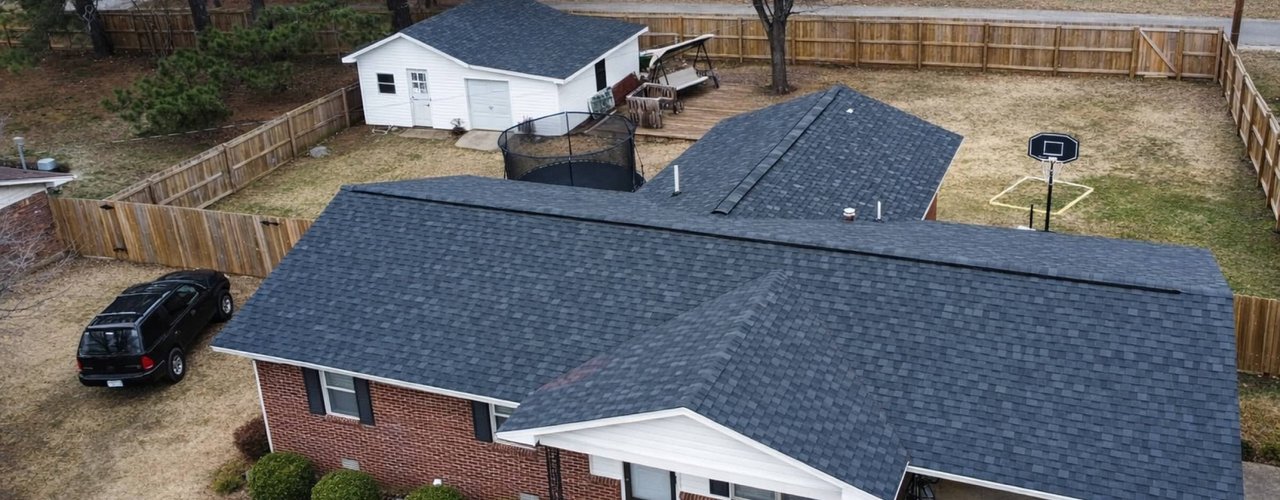 Aerial view of a completed grey shingle roof on a brick ranch home with a new wood privacy fence