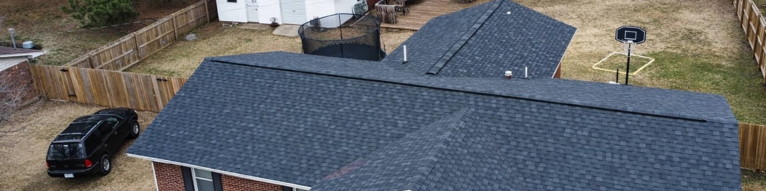Completed charcoal shingle roof on a brick ranch home with a wood privacy fence and detached garage