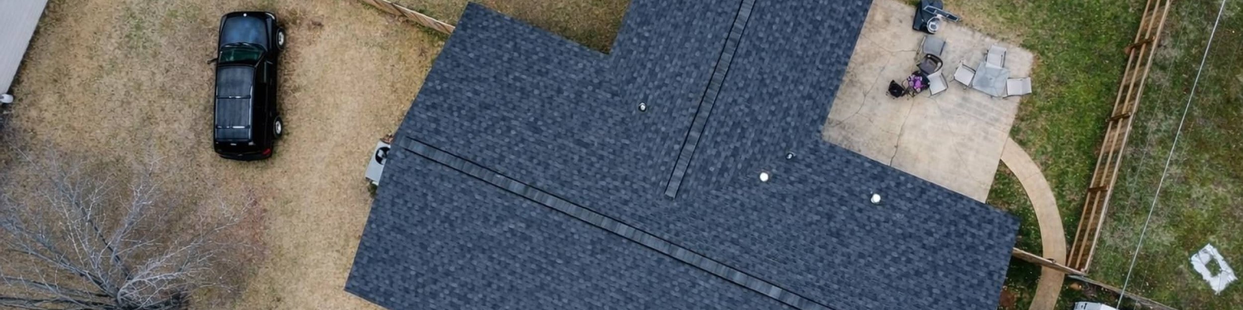 Overhead view of a charcoal shingle roof on a cross-gable home with a large yard