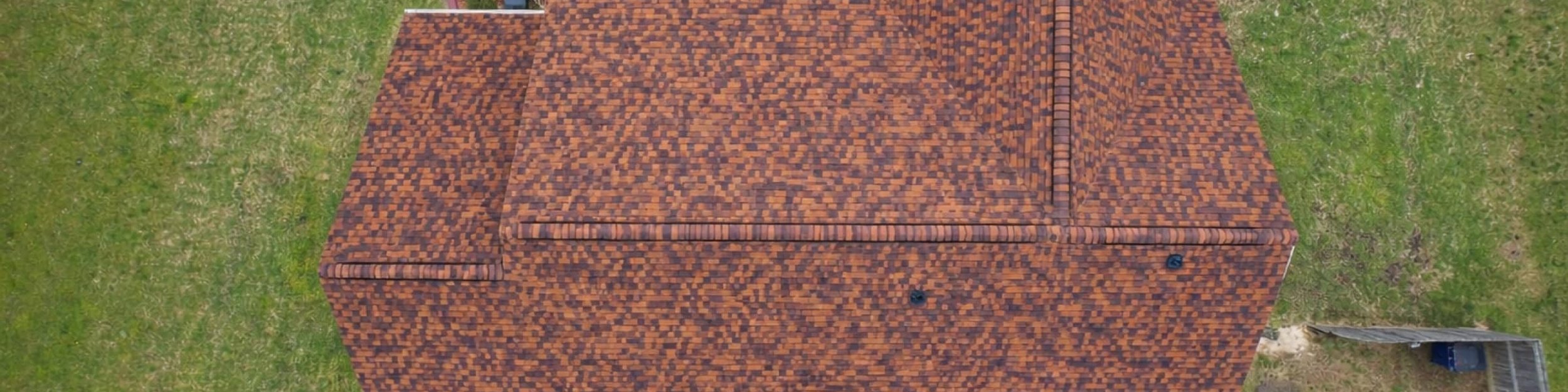 Top-down view of a multicolored brown shingle roof on a home with a large lawn