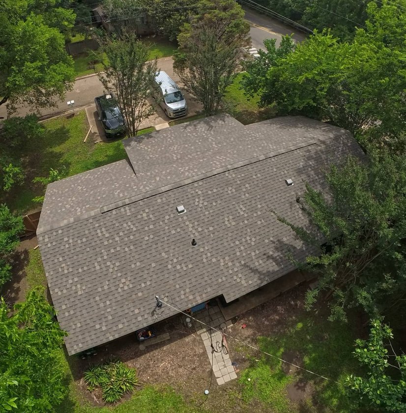 Aerial view of a completed brown shingle roof surrounded by trees in Brandon, MS