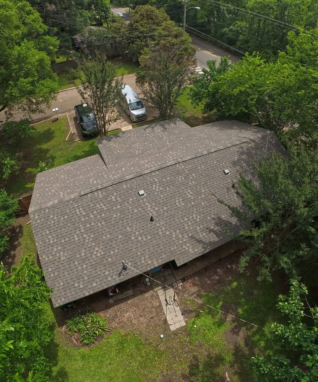 Drone view of a finished brown architectural shingle roof on a single-story home surrounded by tall trees