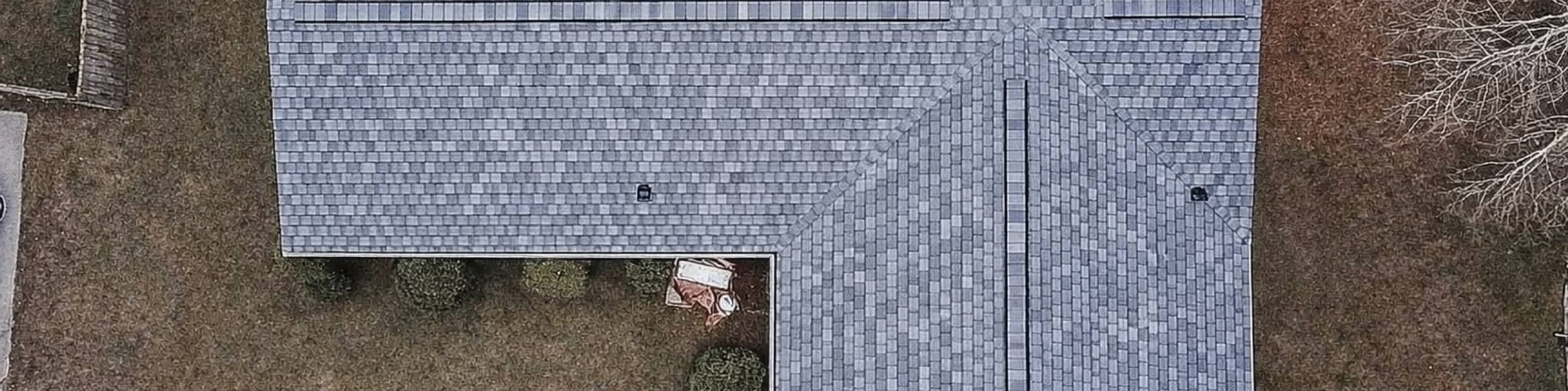 Top-down view of an L-shaped grey shingle roof with roof vents